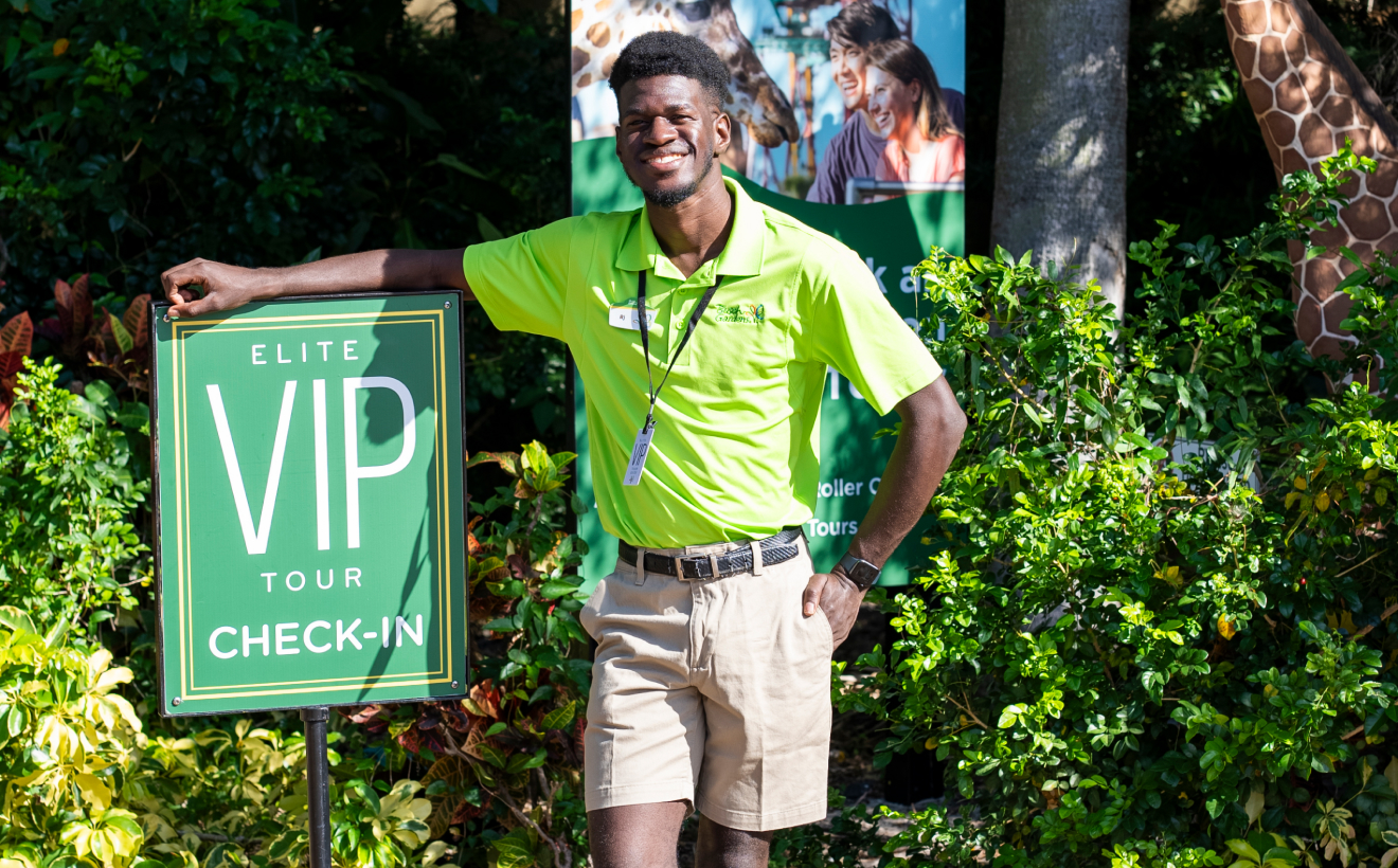 Tour guide in green shirt standing next to Elite VIP Tour sign