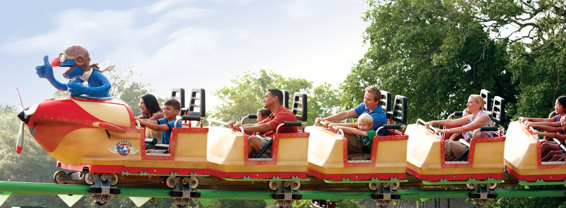 Kids riding a yellow and red roller coaster with adults called Air Grover at Busch Gardens Tampa Bay animal theme park, located in Florida