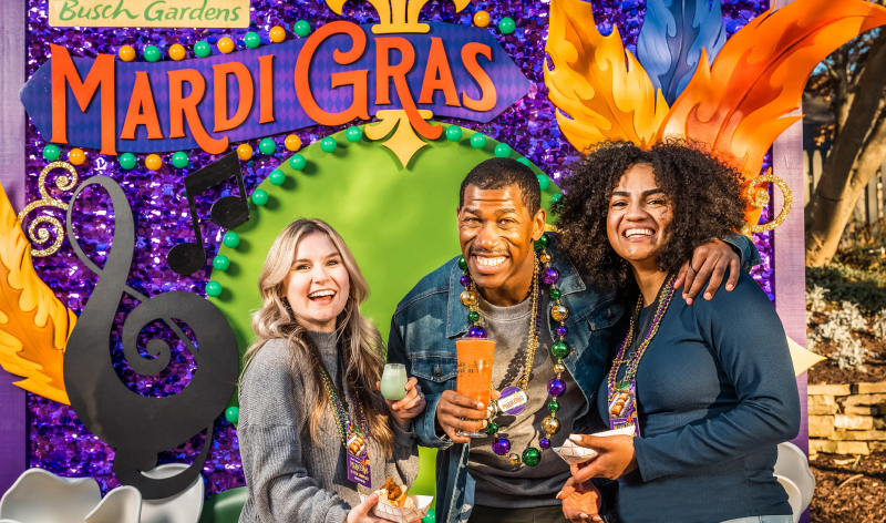 Three adults in front of a Mardi Gras sign