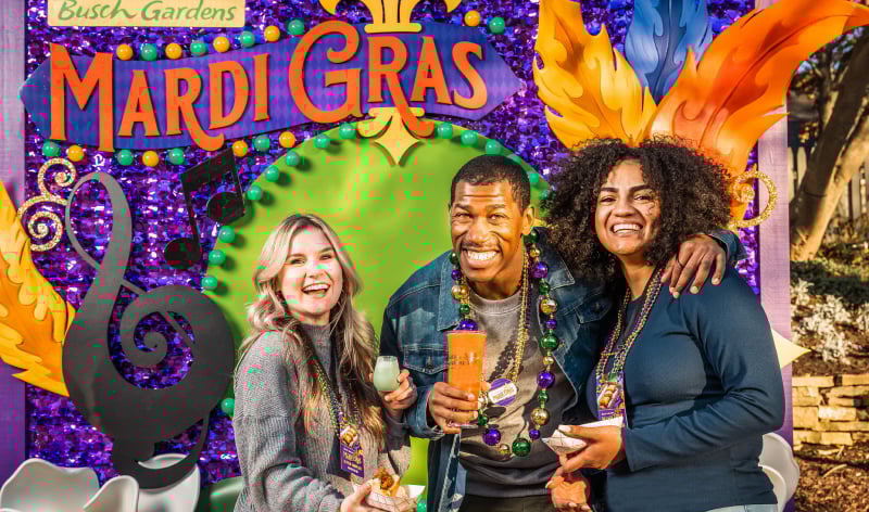 Three adults in front of a Mardi Gras sign
