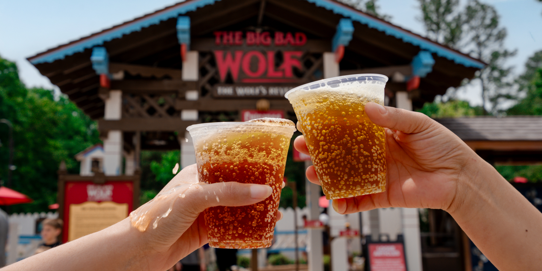 Two hands holding beer in front of an attraction entrance
