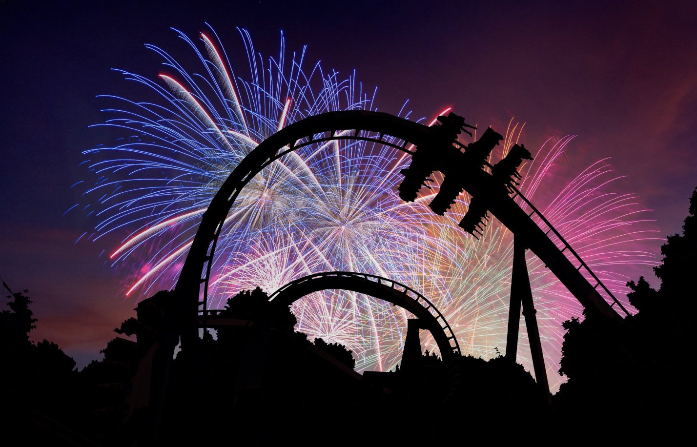 Fireworks at night behind a roller coaster