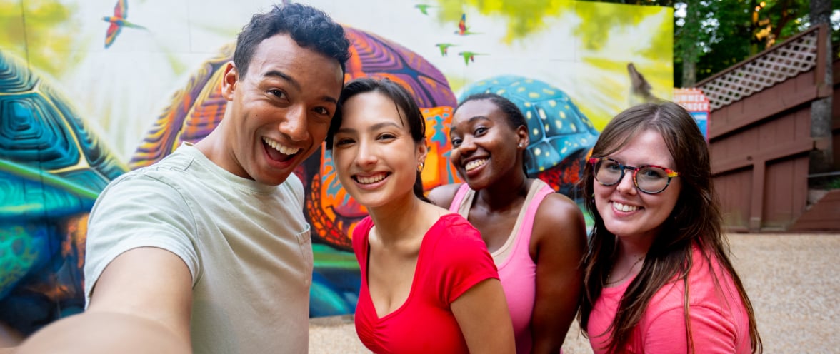 Four people taking a selfie in front of a mural